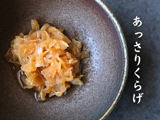 博多久松おせち「博多」弐の重の食材⑯あっさりくらげを別皿にうつして撮影。調味液で黄金色に変色したくらげが小鉢サイズに盛られている。