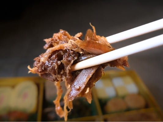 博多久松おせち「博多」参の重の食材㊳牛肉牛蒡しぐれ煮を箸でつまんでいる。牛肉は佃煮のような細切れサイズ。