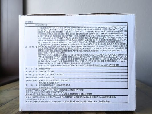 博多久松のおせち「博多」が入った箱を横から撮影。原材料名・内容量・賞味期限などが記載されている。