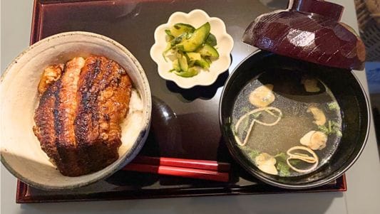 うなぎ丼とお吸い物、きゅうりの漬物がおぼんにのっている。