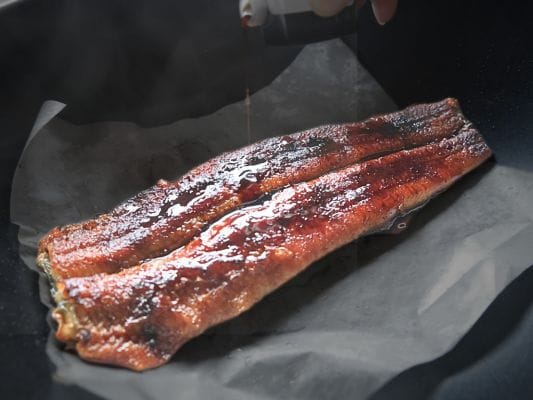 フライパンで焼いている炭焼うな富士「国産青うなぎ長焼き」にたれを掛けている