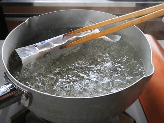 お湯の中にあるスープの袋を箸で裏返しにする