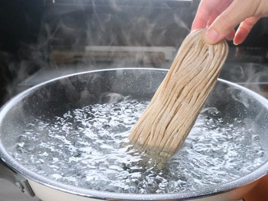 凍った極太麺を大きめの鍋に入れて茹で始める調理シーン