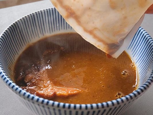 湯煎して温めた濃厚豚骨魚介スープを器に移している様子