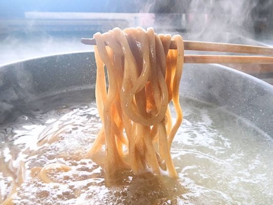 鍋の中から麺を箸ですくっている