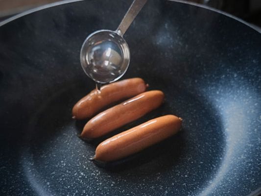 丸大食品の燻製屋熟成あらびきポークウインナーをフライパンにのせて、大さじ1杯の水を入れている。
