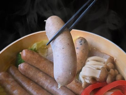 せいろ蒸しにしたヴァイスブルストを箸で持ち上げている。湯気が立っている。
