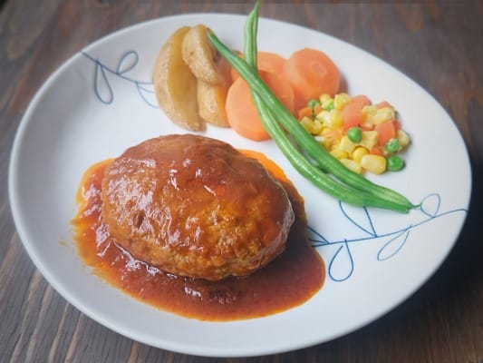 ガスト チーズINハンバーグを野菜とともに皿に盛り付けている