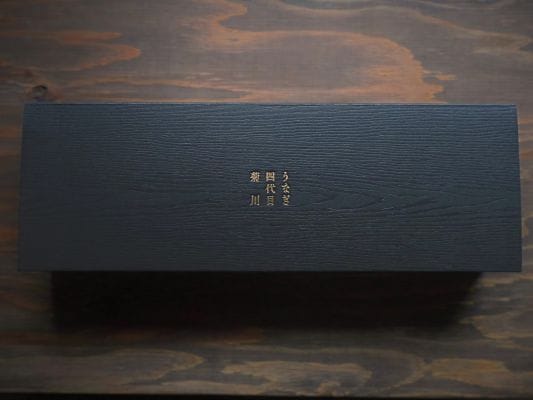 お取り寄せしたうなぎ四代目 菊川「一本うなぎ」の化粧箱。木目調の黒い箱の中央には金色の文字で「うなぎ四代目 菊川」の文字が入っている
