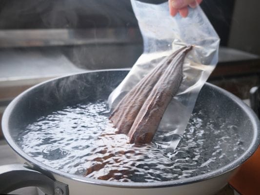お取り寄せしたうなぎ四代目 菊川「一本うなぎ」をたっぷりのお湯が入ったフライパンに冷凍のまま入れている