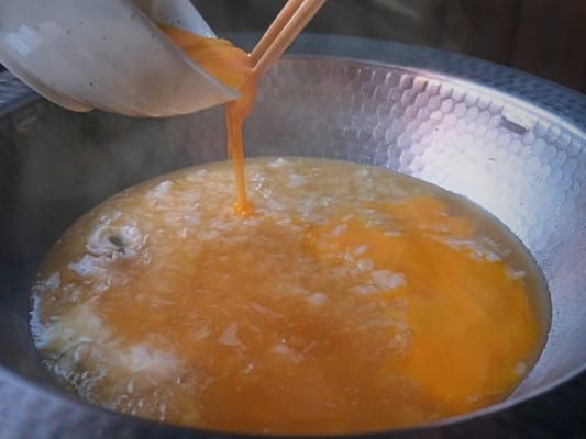ご飯を入れた鍋に溶き卵を回しかけている