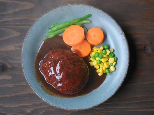 セブンプレミアム 金のハンバーグを野菜とともに皿に盛り付けている