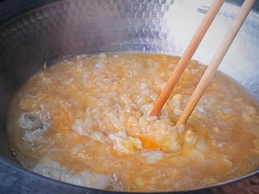 鍋で卵雑炊を調理中。少しずつかたまってきた溶き卵とご飯が混ざり合っている