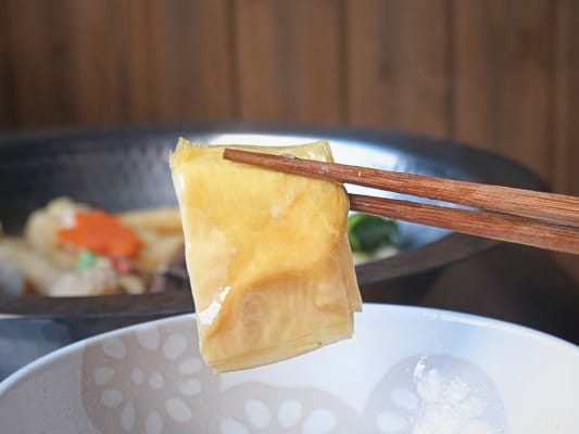 鍋で煮込んだ平湯葉を箸で持ち上げている