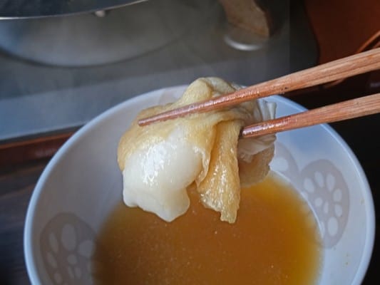 鍋で煮込んだ餅入り巾着を箸で持ち上げている。巾着の中からはとろっとしたお餅が見える
