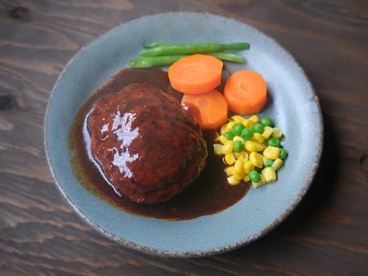 セブンプレミアム ゴールド 金のハンバーグを野菜とともに皿に盛り付けている