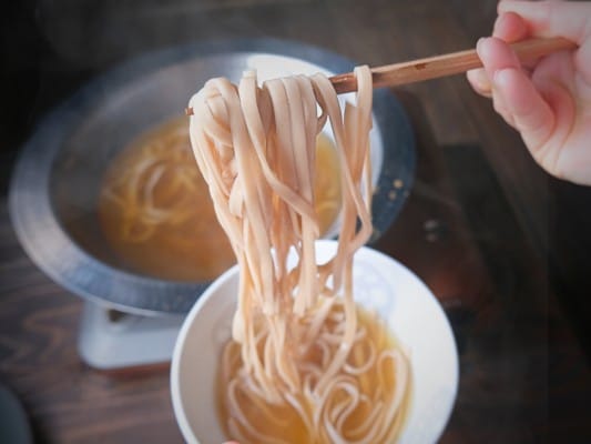 特製だしに入ったれんこん麺を箸で持ち上げている