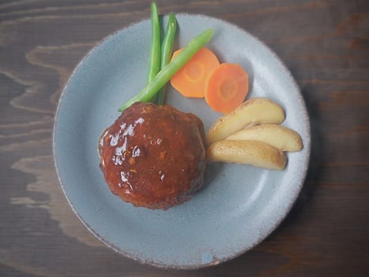 旨包 自家製デミグラスソースハンバーグを野菜とともに皿に盛り付けている