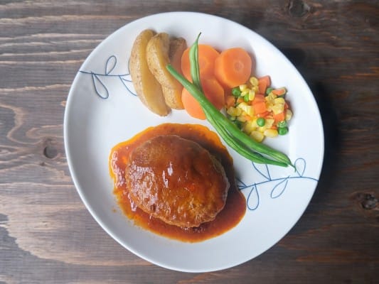 ガストのチーズINハンバーグを野菜とともに皿に盛り付けている