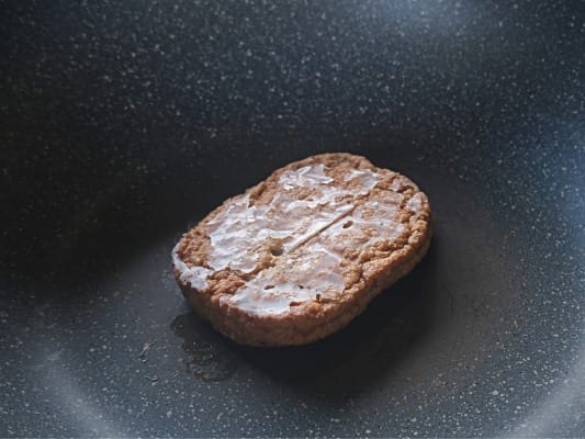 フライパンにのせたマルシンハンバーグ。表面が油脂でコーティングされているため白くなっている