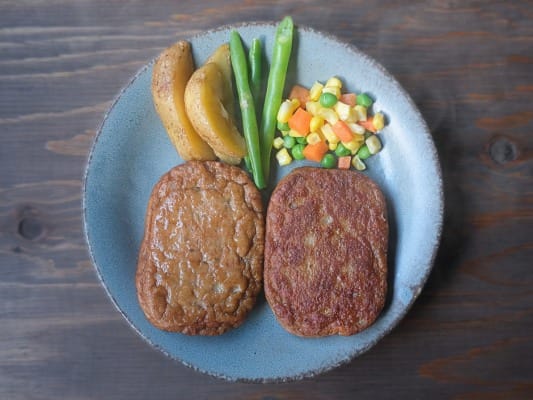野菜とともに皿の上に盛り付けた2枚のマルシンハンバーグ。左がレンジ調理で右がフライパン調理
