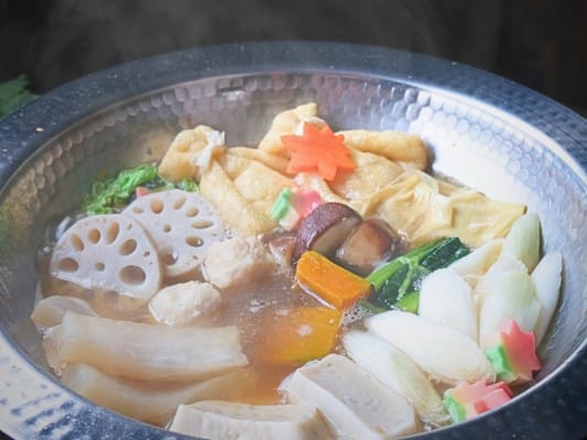 白ねぎや小松菜、大根、れんこん、南京、生麩、餅入り巾着、鶏団子などを鍋に入れて煮ている