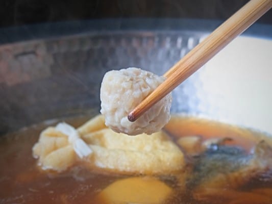 鶏団子を箸で持ち上げ、鍋に入れるところ