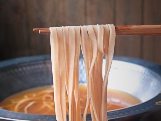 れんこん麺を箸で持ち上げている。きしめんのように麺の幅は広め