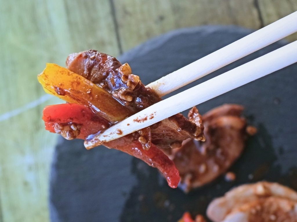 Oisix「本格中華オードブル 慶華2026」の合鴨ロースト 甜麺醤のソースをパプリカと一緒に箸で持ち上げた様子