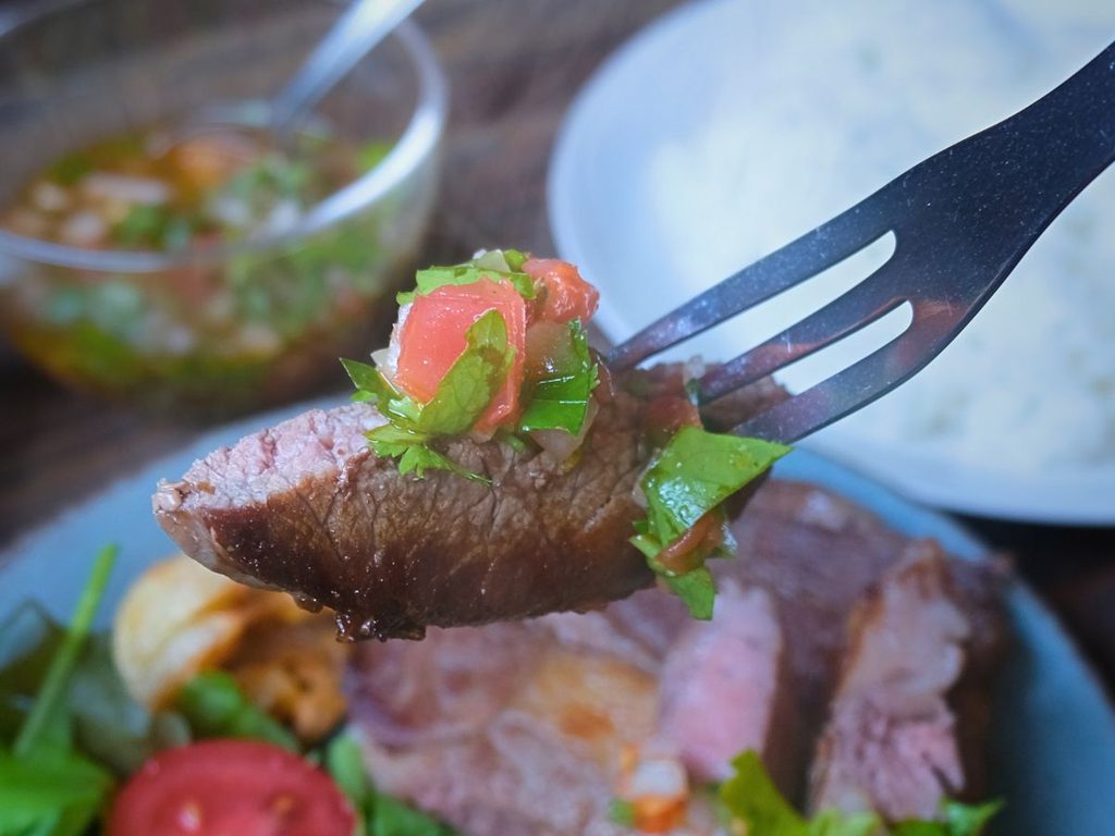 チミチュリソースをのせたアルゼンチン産牛肉リブロースをフォークで持ち上げた様子