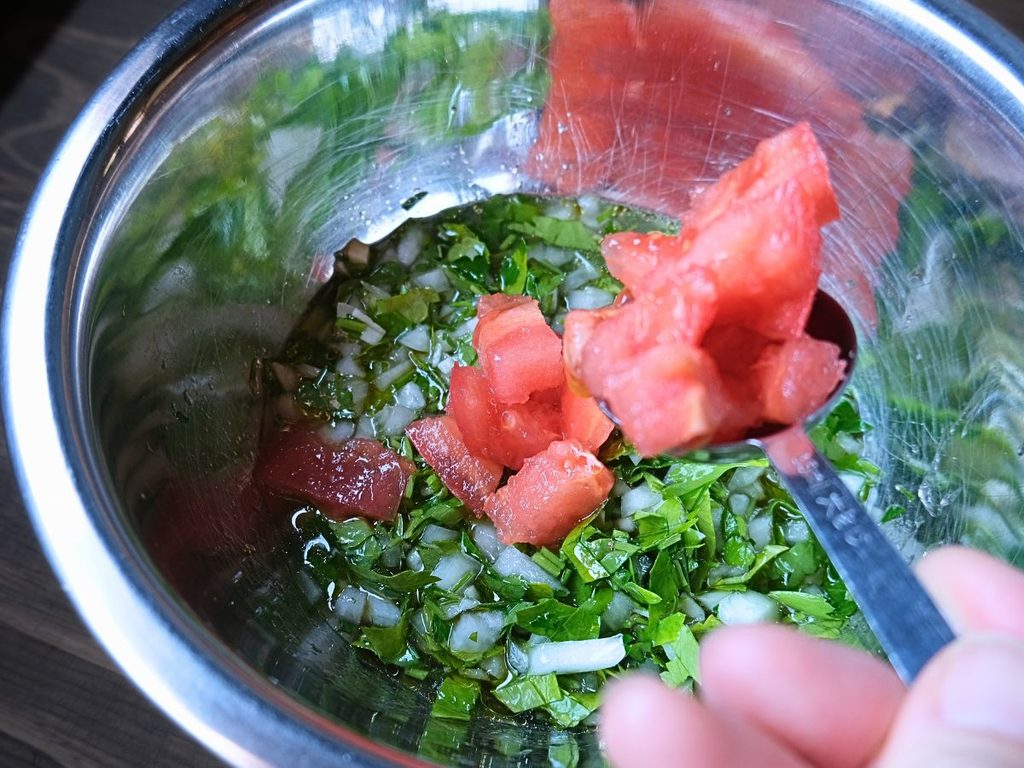 味を見ながらチミチュリソースにトマトを加える様子