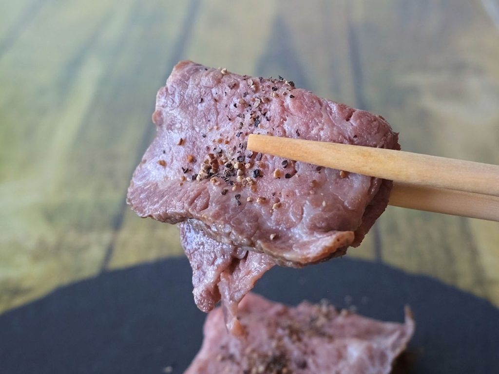 黒胡椒をかけた黒毛和牛ローストビーフを箸で持ち上げた様子