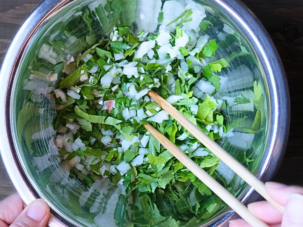 みじん切りにしたパセリ、玉ねぎ、にんにくをボウルで混ぜる様子